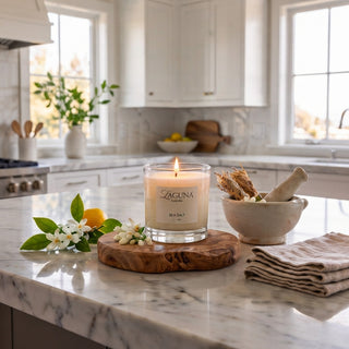 Panel 1: Lit Laguna “PERLOAT” candle on a marble countertop with fresh lemons and white blossoms.
