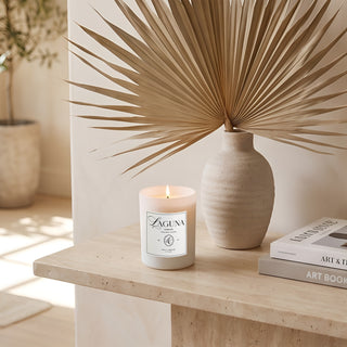Panel 1: Lit Laguna “Tide & Tuberose” candle on a light wooden surface next to a ceramic bowl with dried citrus slices and a smooth stone.   