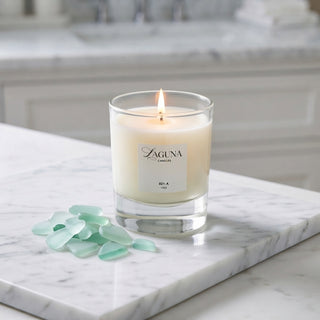 Panel 1: Lit Laguna “821-A” candle on a marble surface next to a cluster of pale green sea glass pieces.