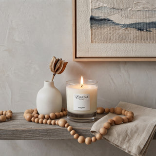 Panel 1: Lit Laguna candle displayed on a rustic wooden table, styled with a white ceramic vase, dried botanical stems, wooden beads, and neutral-toned décor.