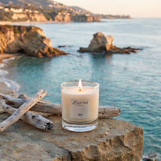 Panel 1: Lit Laguna candle displayed on a natural stone surface overlooking a calm coastal landscape, creating a relaxed seaside setting.