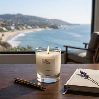 Panel 1: Lit Laguna “Forest Ave.” candle on a wooden desk with a notebook, pen, and a sprig of dried lavender overlooking an ocean view.