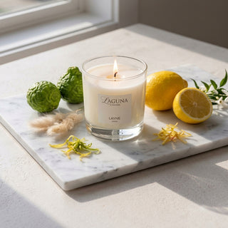 Panel 1: Lit Laguna “Layne” candle with lemons, bergamots, and dried grass on a marble surface.