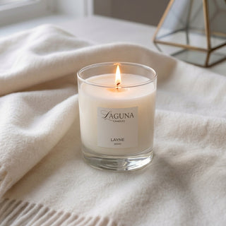 Panel 1: Lit Laguna “Layne” candle on a soft cream blanket with glass terrariums.
